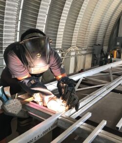 A worker welding metal beams inside a large industrial structure.