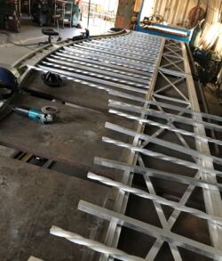 Metal gate with vertical and horizontal bars lying on workshop floor.