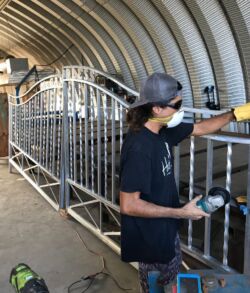 Person assembling a large metal frame inside a curved-roof workshop.