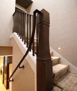A wooden staircase with a dark handrail and beige carpet steps.