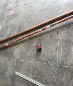 Two copper pipes and a small red valve on a concrete floor.