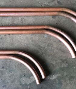 Copper pipes with bent ends laid out on a concrete surface.
