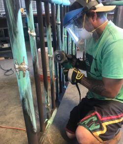 Worker grinding metal bars with protective gear in a workshop.