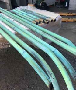 Stack of long green metal pipes with curved ends on a workshop floor.