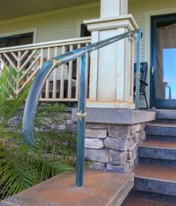 Outdoor metal handrail with a curved design beside stone steps.