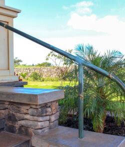 Curved metal handrail on outdoor stone steps with greenery in the background.