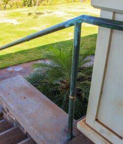 Rusty metal railing and concrete stairs outdoors in a sunny area.