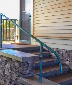 Curved metal handrail beside stone steps leading to a porch.