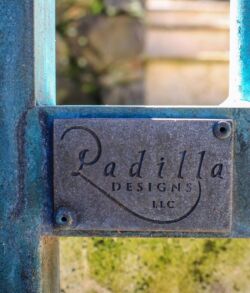 A metal nameplate with 'Padilla' attached to a blue gate.