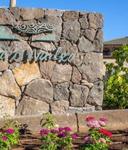Stone sign reading 'La Madera' with flowers and houses in the background.