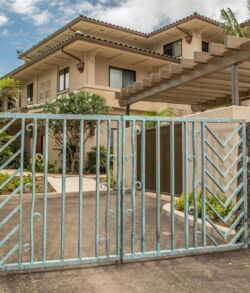 Modern two-story house with a gated driveway and lush greenery.