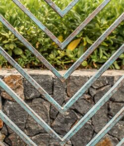 Close-up of a metal gate with geometric patterns in front of green foliage.