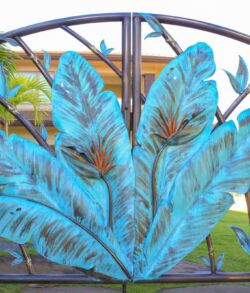Blue leaf-shaped metal art on a fence with a garden background.