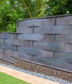Modern metal fence panels with a textured finish in a garden setting.