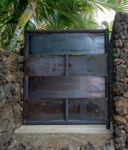 Rustic metal gate set between stone walls and tropical plants.