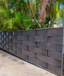 Modern black metal fence with a geometric pattern in a tropical setting.