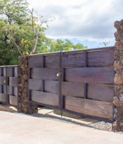 Rustic wooden gate with stone pillars in a natural setting.