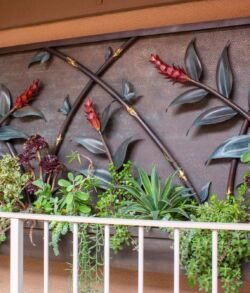 Decorative metal wall art featuring branches and birds above green plants.
