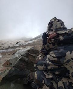 Person in camouflage jacket taking a photo near foggy mountains.