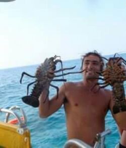 Man holding two large lobsters on a boat at sea.
