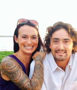 A smiling couple posing outdoors near water.