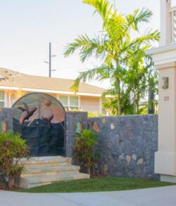 Decorative stone wall with a bird mural and palm trees in a sunny yard.
