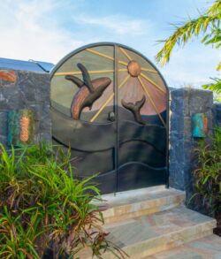 Decorative metal gate featuring sun and bird designs at a garden entrance.