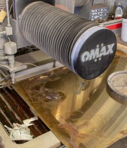 An OMAX waterjet cutting machine nozzle above a metal sheet.