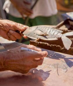 Hands carving intricate designs into wood using a chisel.