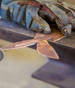 Handcrafted metal leaf decoration and worn gloves on a wooden surface.