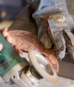 A person uses a power tool to shape a wooden object held by a gloved hand.