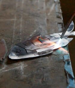 A fish grilling on a metal surface with a spatula nearby.