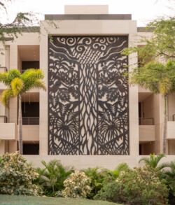 Intricate tree mural on a building facade surrounded by greenery.