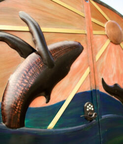 Copper and brass man gate Sculpture of a whale breaching with a sun motif in the background.