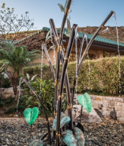 Copper and brass water feature Decorative garden sculpture with metal branches and green leaves under a sunny sky.