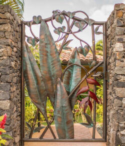 Copper floral design A decorative metal gate with cactus and heart designs between stone pillars.
