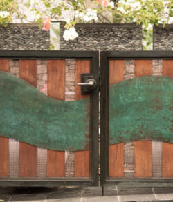 Copper wood and brass gate double swing man gate. Rustic metal gate with green patina and brick wall behind.