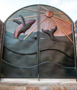 Metal gate with dolphin and sun design at sunset.
