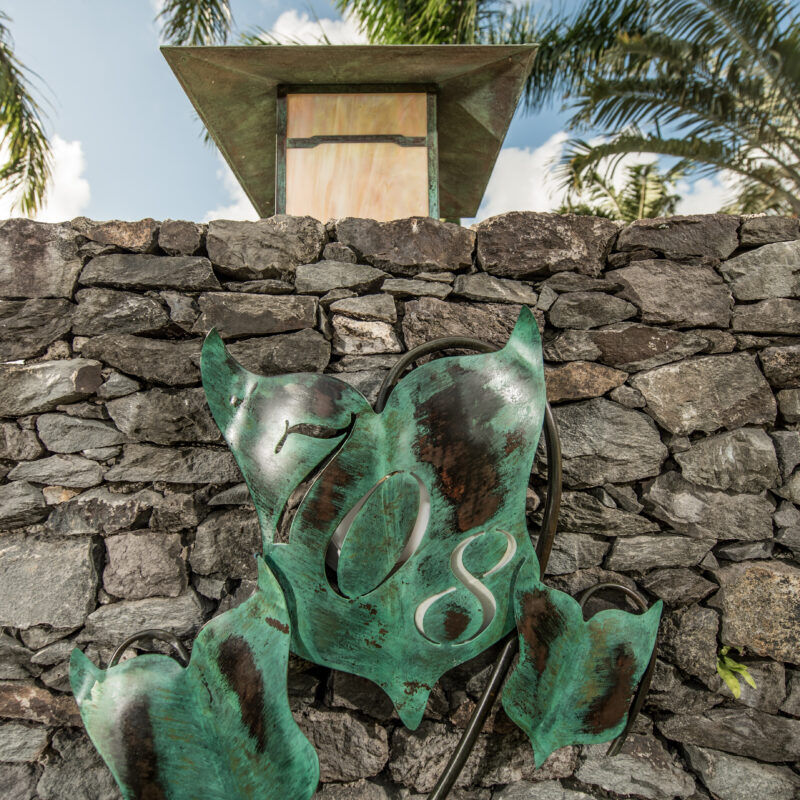 Abstract green sculpture in front of a stone wall under a small monument.