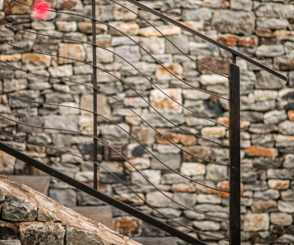 Stone staircase with metal railing against a rustic stone wall.
