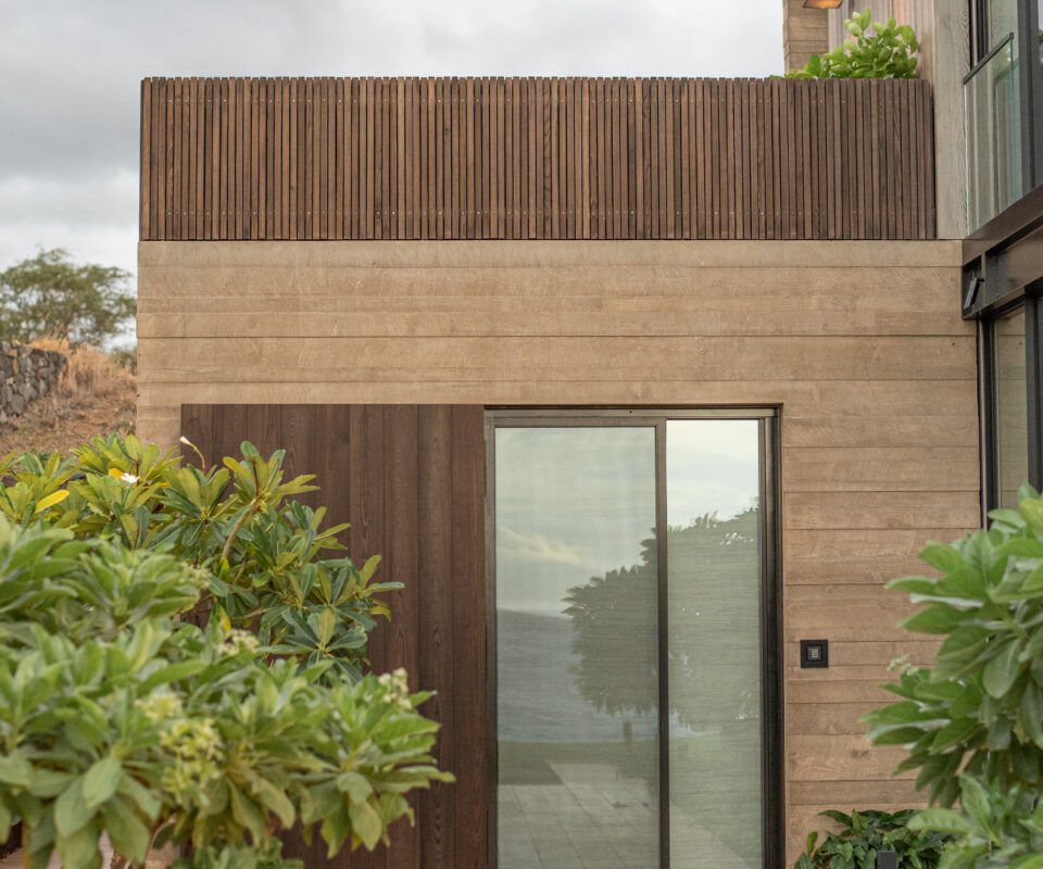 Modern building entrance with wood and glass details surrounded by greenery.