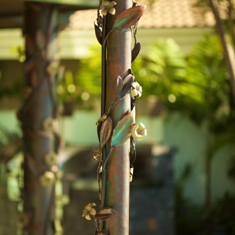 A close-up of a metal pole with ornamental rings and blurred greenery in the background.