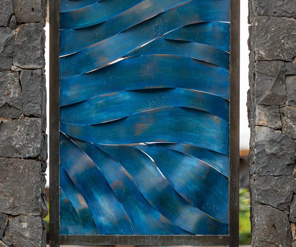 Abstract blue metal sculpture with wavy patterns framed by stone pillars.