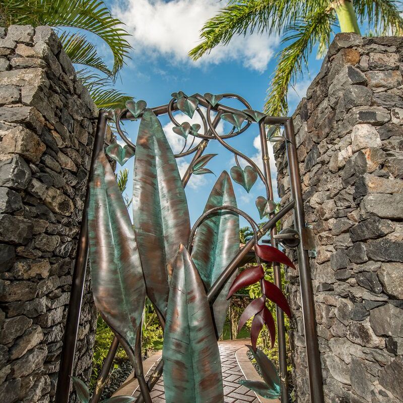 Artistic metal gate between stone pillars under palm trees.