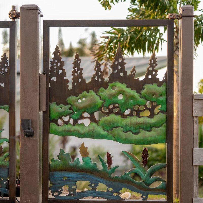 Decorative metal gate featuring a nature scene with trees, birds, and water.