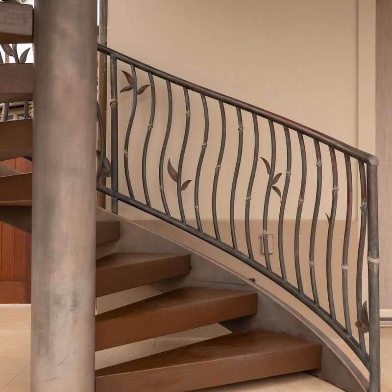 Curved wooden staircase with wrought iron railing and vertical pillar.