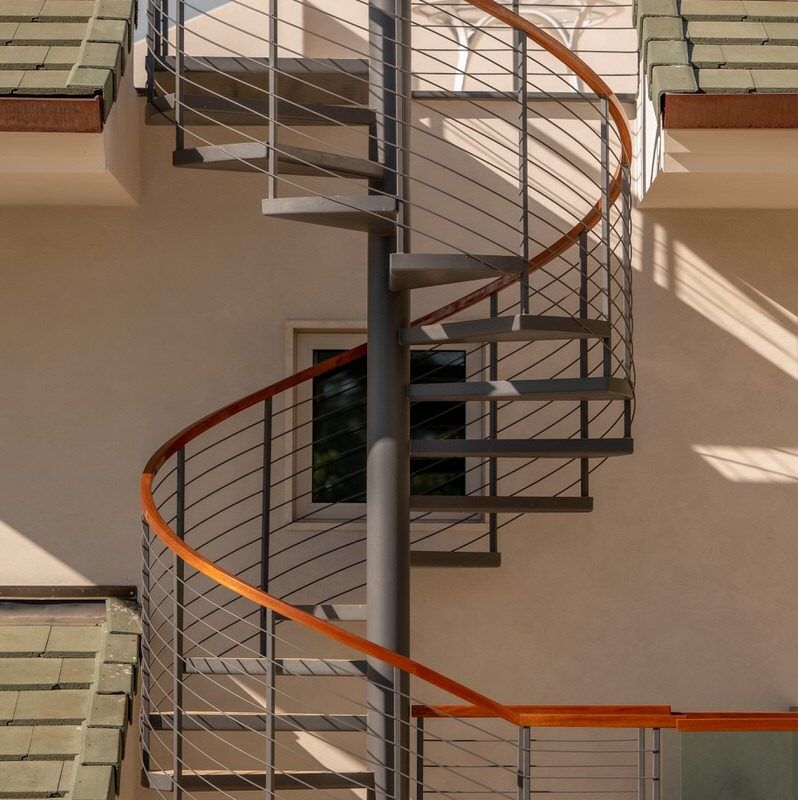A modern spiral staircase with metal steps and wooden handrails against a beige wall.