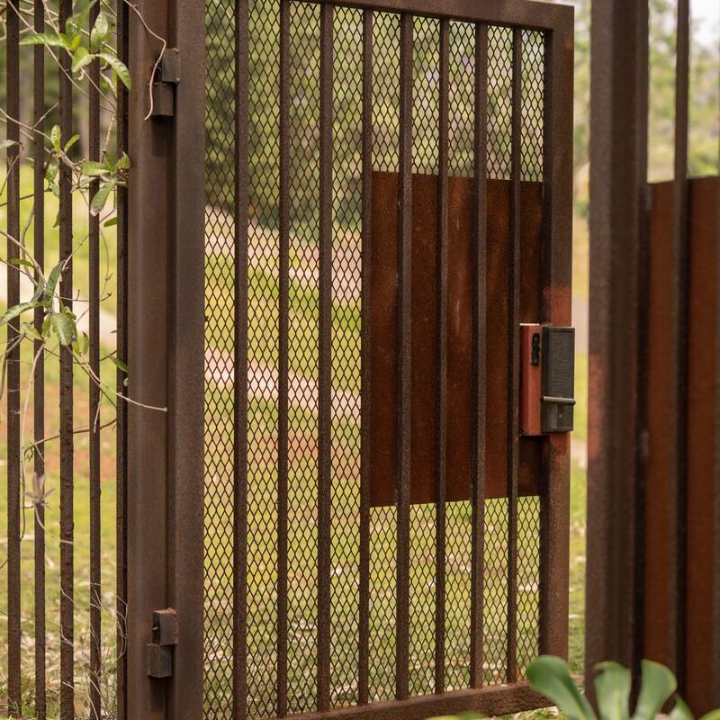 A metal gate with mesh and a keypad lock in an outdoor setting.