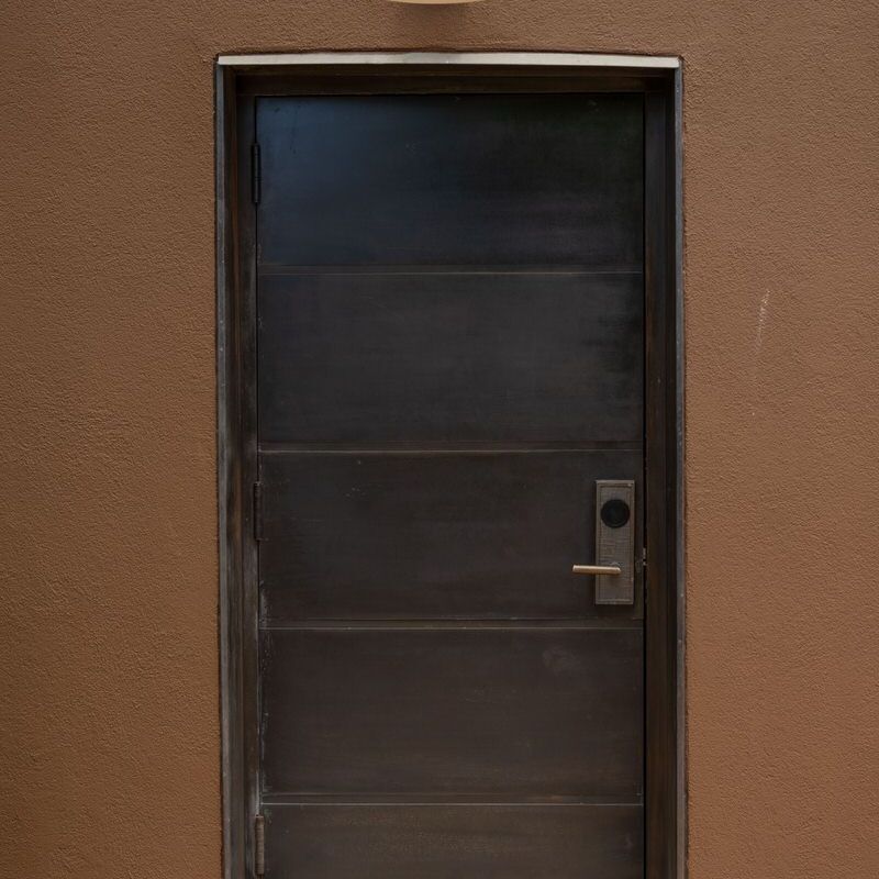 A black metal door set in a plain brown wall.